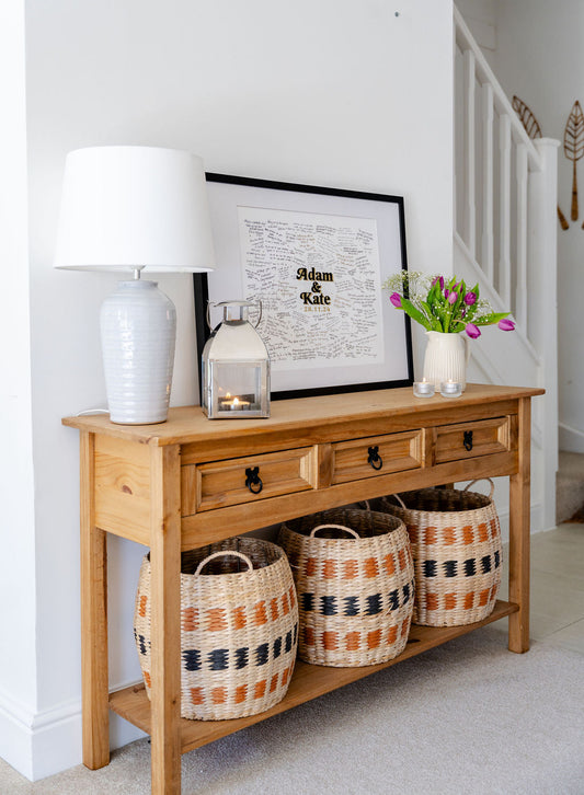 A medium sized Mr & Missive guest book alternative on a sidetable surrounded by a lamp, candle and fresh flowers