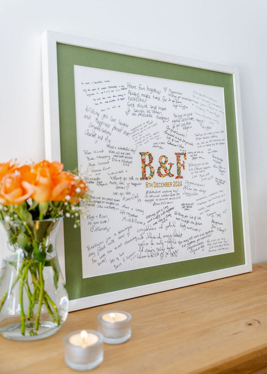 A Mr & Missive wedding guest book alternative with a handstitched centrepiece and the guest's messages arranged around it, placed on a sideboard with fresh flowers and lit candles