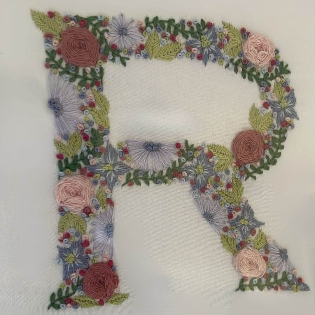 Close up of a hand-embroidered letter R from the centrepiece of a Mr & Missive Floral Collection wedding guest book alternative.