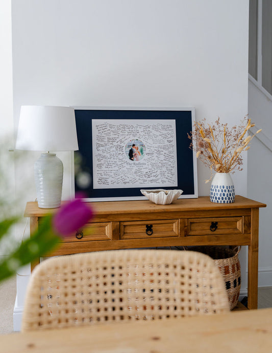 A Mr & Missive wedding guest book alternative, placed on a sideboard with flowers and a side lamp