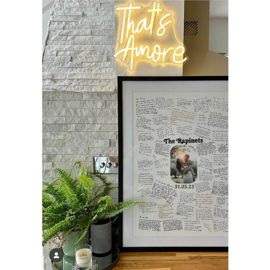 A handwritten Mr & Missive wedding guest book alternative from the Portrait Collection, featuring a photograph of a bride and groom with their name and wedding date either side, positioned against a wall with a plant in the foreground.