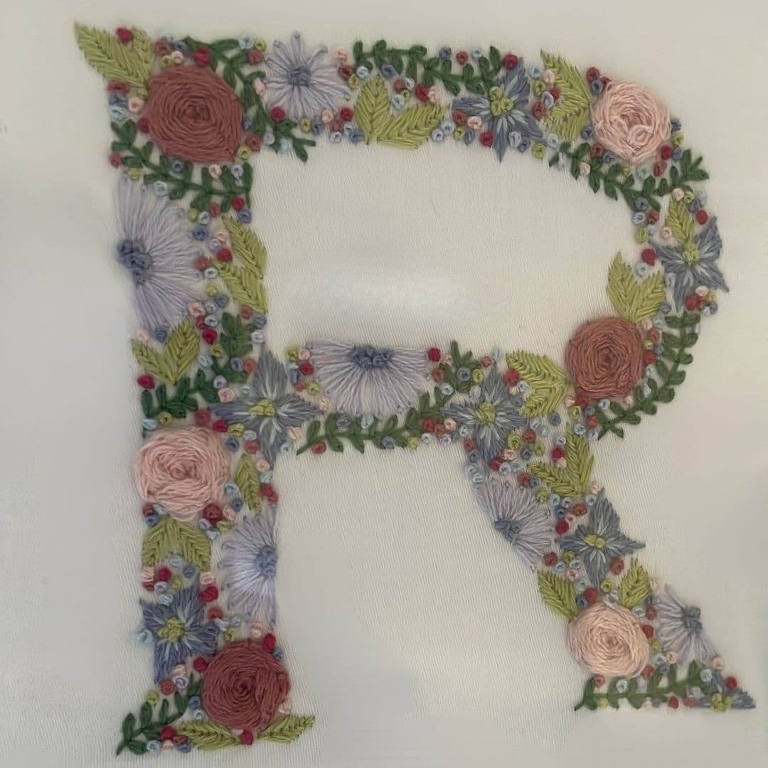 Close up of a hand-embroidered letter R  from the centrepiece of a Mr & Missive Floral Collection wedding guest book alternative.